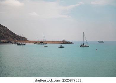 A peaceful harbor scene featuring several boats anchored in calm, turquoise waters under a serene blue sky, with a rocky coastline in the background. - Powered by Shutterstock