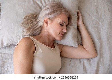 Peaceful Healthy Beautiful 50s Mature Woman Lying Asleep On Comfortable Pillow Orthopedic Mattress Sleeping Well In Cozy Bed Alone, Calm Serene Old Female Resting In Bedroom, Close Up Top View