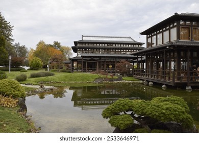 A peaceful Japanese garden with a pond reflecting traditional wooden buildings. Surrounded by greenery and autumn leaves, the scene captures the calm and beauty of Japanese architecture and nature. - Powered by Shutterstock