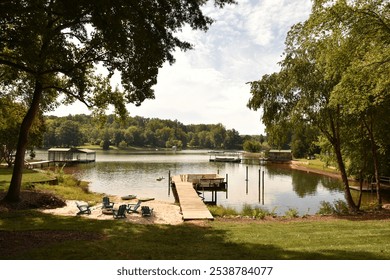 A peaceful lake with a wooden pier stretching over calm waters. Beside it lies a small sandy beach with a cozy resting area, complete with benches and shaded spots - Powered by Shutterstock