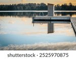 A peaceful lakeside landscape with a wooden pier stretching out into the calm water and reflecting the golden hues of the sunset. A small staircase and a floating platform add to the peaceful atmosphe