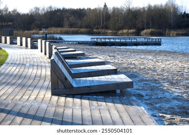 Peaceful lakeside scene featuring modern wooden benches along a boardwalk, adjacent to a sandy beach with calm water. Perfect for relaxation and enjoying nature's tranquility. - Powered by Shutterstock