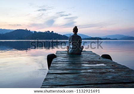 Peaceful lifestyle shot of woman sitting on dock at sunset on Lake Bunyonyi, Uganda, Africa.