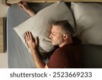 Peaceful middle aged man lying in comfy bed taking nap, sleeping male hugging pillow, above view. Healthy rest routine