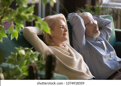 Peaceful middle aged man and woman with closed eyes relaxing on comfortable couch at home, mature family daydreaming together, grey haired wife and husband resting with hands behind head, breathing - Powered by Shutterstock