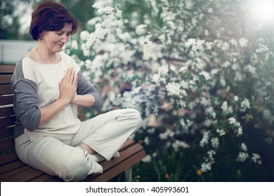 peaceful middle-aged woman meditating in the garden with her palms in namaste - Powered by Shutterstock