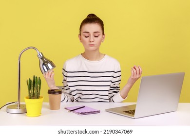 Peaceful mind, break at work. Calm woman sitting at workplace with laptop and raising hands in mudra gesture, meditating resting at home office. Indoor studio studio shot isolated on yellow background - Shutterstock ID 2190347069