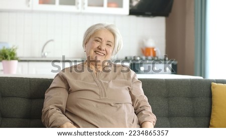 Peaceful old woman resting in her quiet home.Lonely old woman sitting alone on sofa in her peaceful home. She is smiling at the camera. Portrait of happy old woman.