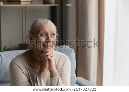Peaceful older woman resting alone at home, having nostalgic mood looking serene, recollect memories sits on couch, smile staring out window feels satisfied, enjoy carefree life on retirement concept