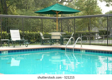 Peaceful poolside scene, with umbrella, table, and chairs.