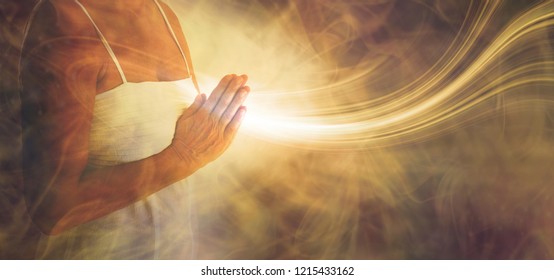 Peaceful prayer sending love and light out -  female in white dress with hands in prayer position and a stream or white light flowing outwards with a rustic golden brown ethereal energy background
