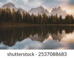 Peaceful reflections of autumnal trees and the Cadini di Misurina mountains at dawn over the calm waters of Lago d