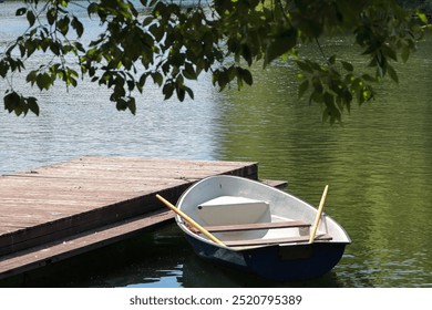 A Peaceful Scene Of A Lone Rowboat Moored Beside A Wooden Dock On A Calm, Green Lake. The Perfect Depiction Of Tranquility And Nature's Simplicity. - Powered by Shutterstock