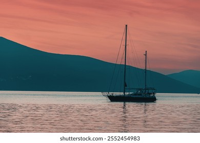 Peaceful scene of a sailboat anchored in calm waters with a beautiful sunset and mountains in the background - Powered by Shutterstock