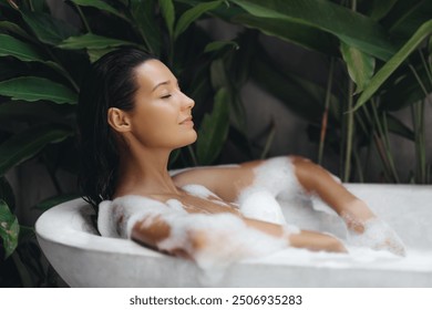 A peaceful scene of a woman enjoying a luxurious bath in an outdoor tub, surrounded by vibrant tropical plants. This image evokes a sense of relaxation and self-care, ideal for spa and wellness - Powered by Shutterstock