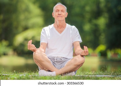 Peaceful senior man meditating seated on a blanket in a park by a lake - Powered by Shutterstock