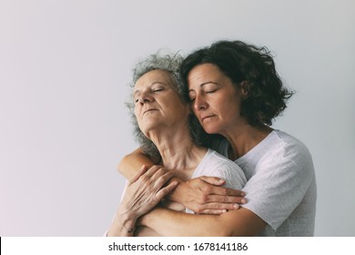 Peaceful serene adult daughter hugging senior mother. Middle aged woman with closed eyes embracing elderly lady. Family bonds concept