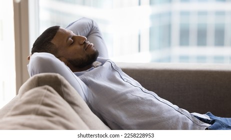 Peaceful sleepy handsome Black guy relaxing on soft couch, leaning on back, holding nap with closed eyes, taking deep breath of fresh air, enjoying leisure, break, pause, weekend. Banner shot