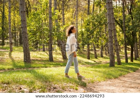 Peaceful and smiling young woman is walking in summer sunlight in the green woods.