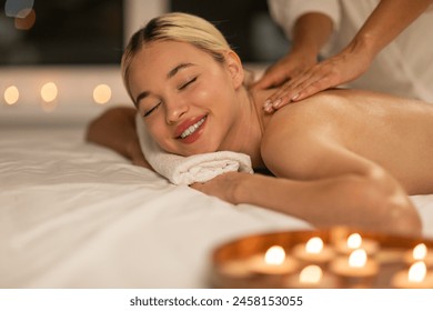 In a peaceful spa environment, a young blonde woman experiences a therapeutic back massage, the setting evoking a sense of serenity and well-being - Powered by Shutterstock