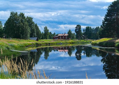 A peaceful summer lake view of Swedish countryside in Dalarna. There is a traditional stuga - red country house in the background  and a reflection on the water