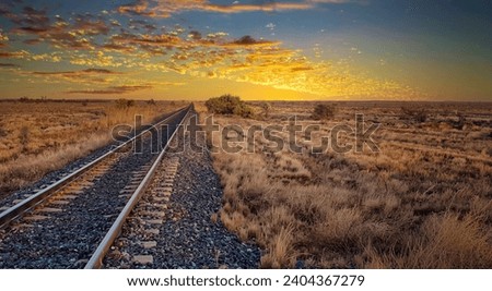 Peaceful sunrise over a vast open field with railroad tracks.
