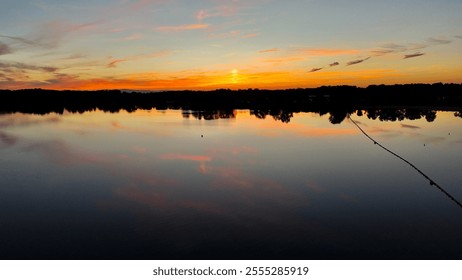 A peaceful sunset scene over a calm lake, with vibrant colors reflecting on the water and silhouettes of distant trees creating a serene atmosphere - Powered by Shutterstock