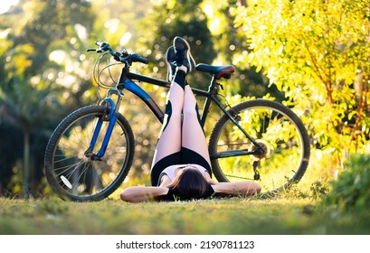 Peaceful Woman Lying On The Grass To Rest With Her Legs Propped Up On Her Bicycle.