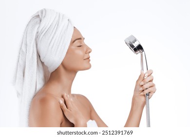 A peaceful woman with a towel wrapped around her head holds a showerhead, embracing a moment of calm and relaxation. Perfect for illustrating concepts of self-care, beauty, and personal hygiene. - Powered by Shutterstock