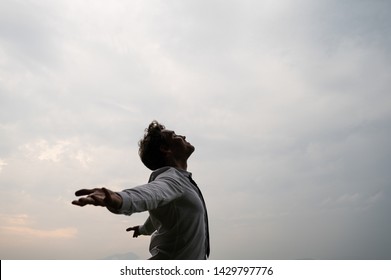 Peaceful young businessman standing with his arms spread looking up towards a cloudy sky.