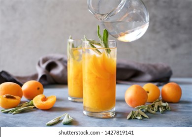 Peach Or Apricot Nectar With Sage In Glass. Female Hands Add Water From Jug