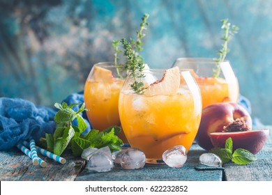 Peach cocktail or tea with ice and thyme on blue background.