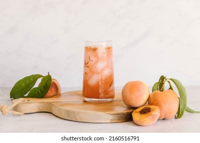 A Peach drink in a glass with ice in a marble kitchen. There are also fresh fruit, some cut up. The drink is on a brown cutting board, ready to serve.  - Shutterstock ID 2160516791