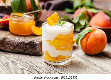 Peach fruit dessert in glass cup on rustic wooden table with fresh peach fruit, peach jam. Homemade dessert with fruits. Fruit salad with yogurt or sour cream.