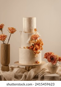 Peach fuzz coloured wedding cake decorated by flowers standing on table 