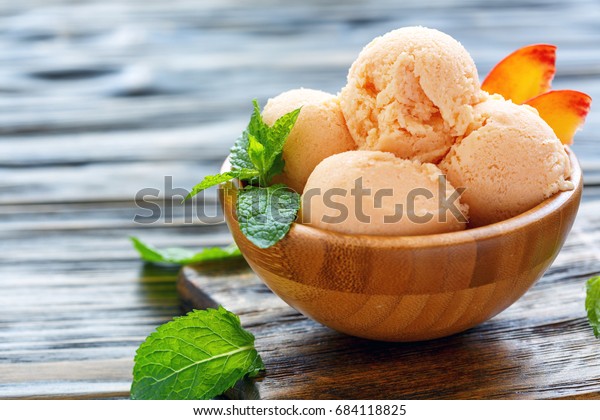 Peach ice cream, peach slices and mint
leaves wooden bowl on old table, selective
focus.
