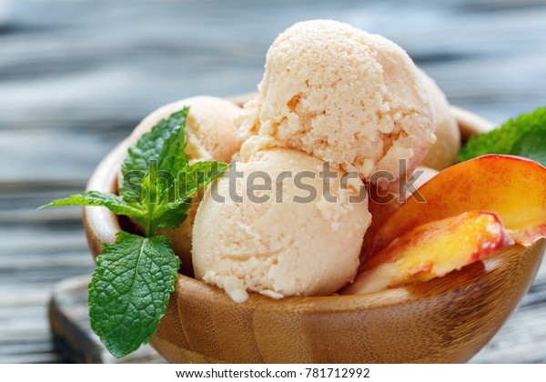 Peach ice cream, peach slices and mint\
leaves wooden bowl on old table, selective\
focus.