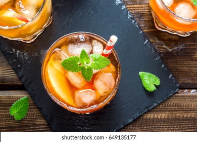 Peach iced tea. Iced tea with peach slices, mint and ice cubes on slate and wooden rustic background close up. Homemade refreshing summer drink.