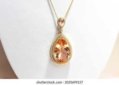 Peach precious gemstone morganite in oval shape pendant golden rose necklace with small diamond stones gems on retail display easel with white background in jewelry store shop - Shutterstock ID 2035699157