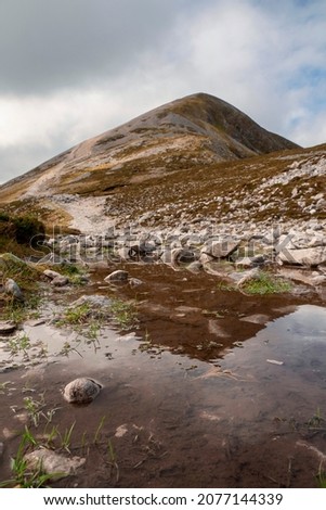 Peak of Croagh Patrick reflection in a paddle of water. Popular landmark for pilgrimage and hiking. County Mayo, Ireland. Clean cloudy sky. Small narrow foot path leads to the top