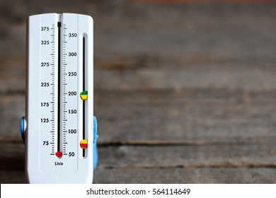 Peak Flow Meter Isolated On Wood Background. Hand Medical Device Used To Monitor Breath Of A Person Bronchial Asthma Suffering. Peak Flow Meter Wide Range Of Values. Breath Test Allergy. Lung Testing