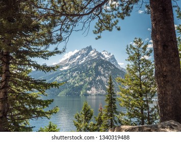 A peak of the Grand Teton mountain range, set upon the stills waters of Phelps Lake, Grand Teton National Park, Wyoming, USA. The snow dappled mountain is framed by the green pine forests.