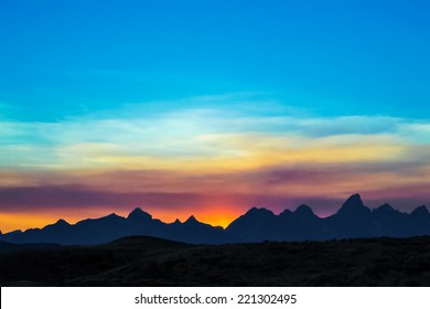 The peaks of the Cathedral Group of the Teton Mountain Range, near Jackson Hole, Wyoming, are silhouetted by a colorful sky at sunset. Grand Teton National Park.