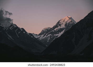 The peaks of Mount Cook are illuminated by the warm glow of sunset, with snow-capped mountains contrasting against a pastel sky. The alpine landscape is serene and majestic. - Powered by Shutterstock