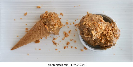 Peanut Butter Banana Ice Cream Scoops Of Ice-cream In A White Bowl/cup And Gluten-free Waffle Cone With Sprinkles Of Peanuts On Top On A White Table. View From Above Top View