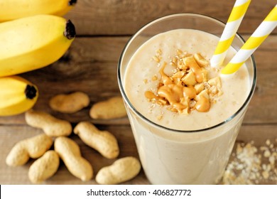 Peanut Butter Banana Oat Smoothie With Paper Straws On Rustic Table With Scattered Ingredients