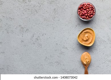 Peanut butter in bowl and spoon and bowl with peanuts on concrete background, top view, copy space. Artisan peanut butter concept
