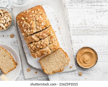 Peanut butter cake sliced on wooden cutting board. Homemade cake with peanut flour, cinnamon decorated with chopped nuts and sugar. Top view. Copy space. White wooden table. - Shutterstock ID 2162591015