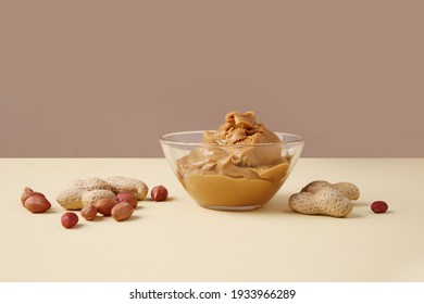 Peanut butter in a glass bowl with nuts scattered on the table. Colored background. Copy space for your text