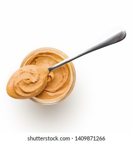 Peanut butter in glass jar and spoon isolated on white background, top view, copy space. American dessert concept